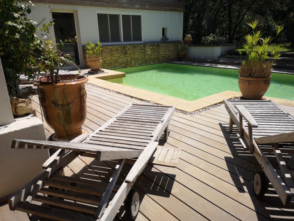 Terrasse en bois ipé avec piscine, tarusate au soleil avec deux gros pot de fleurs, maison en arrière plan